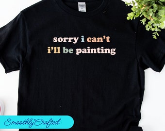 May include: Black t-shirt with the text "sorry i can't i'll be painting" in rainbow colors.