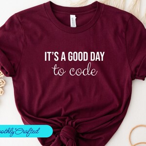 Puede incluir: Camiseta color burdeos con texto blanco que dice "Es un buen día para programar".