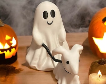 May include: A white ghost figurine with a friendly face and a black leash attached to a white ghost dog figurine. The ghost dog has a black eye and a black nose.