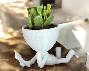 Maceta con forma de bibliotecario filósofo leyendo un libro: un tipo inteligente tumbado en el suelo con un libro. Maceta única para suculentas, ideal para decorar el escritorio o la oficina.