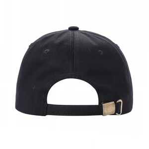 May include: Black baseball cap with a curved brim and adjustable strap. The cap features a brass-colored metal buckle for size adjustment. The back of the cap is visible against a white background.