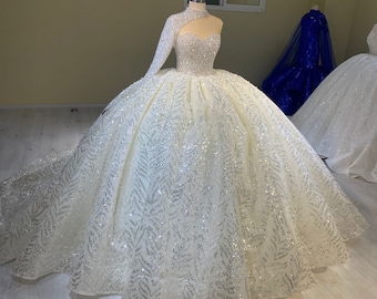 May include: A white wedding dress with a long, flowing skirt and a fitted bodice. The dress is covered in silver sequins and has a one-shoulder design.