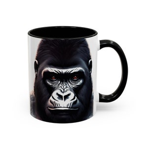 May include: A white ceramic mug with a black rim and handle. The mug features a close-up image of a gorilla's face with intense red eyes.