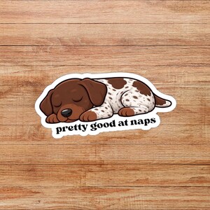 Puede incluir: Una pegatina con un cachorro de dibujos animados durmiendo. El cachorro tiene pelaje marrón y blanco moteado y está acostado. El texto "pretty good at naps" está debajo del cachorro en blanco.