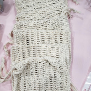 Puede incluir: Varias bolsas de tejido abierto de color blanquecino con cierres de cordón. Las bolsas están apiladas unas sobre otras, con los cordones colgando. Las bolsas parecen estar hechas de fibra natural.