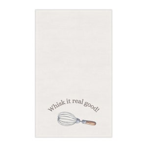 Puede incluir: Paño de cocina color crema con una ilustración de un batidor y la frase "Whisk it real good!" en gris. El batidor tiene un mango de madera.