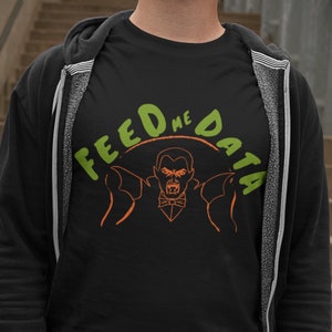 May include: A black t-shirt with a green and orange graphic of a vampire with the text "Feed Me Data" around the vampire.