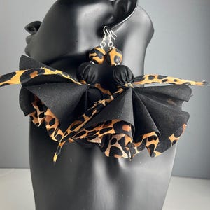 May include: Black and leopard print fabric earrings with a matching collar. The earrings have a beaded design with a leopard print pattern. The collar is made of black fabric with leopard print accents.