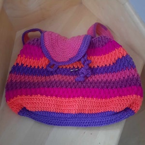 May include: A colorful crocheted backpack with a pink, orange, purple, and blue striped pattern. The backpack has a flap with a small buckle.