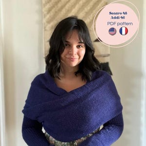 Peut inclure: Une femme porte un châle tricoté bleu foncé avec des manches longues. Le châle est enroulé autour des épaules et des bras. L'image comprend le texte "Sentro 48 Addi 46 PDF pattern" avec des drapeaux américain et français.