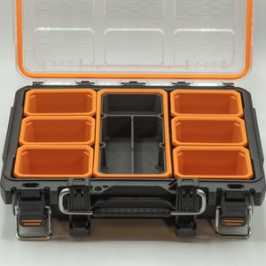 Puede incluir: Una caja de herramientas de pl&aacute;stico negra con un borde naranja y varios compartimentos extra&iacute;bles. La caja de herramientas est&aacute; abierta y los compartimentos est&aacute;n vac&iacute;os.