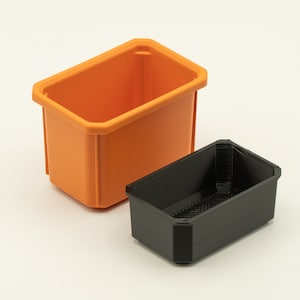 May include: Two plastic storage containers, one orange and one black. The orange container is larger and is sitting on a white surface. The black container is smaller and is sitting inside the orange container.