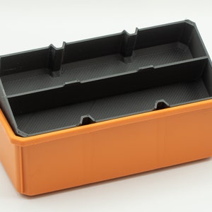 Puede incluir: Una caja de almacenamiento de pl&aacute;stico naranja con un inserto de pl&aacute;stico negro que tiene divisores. La caja est&aacute; vac&iacute;a.