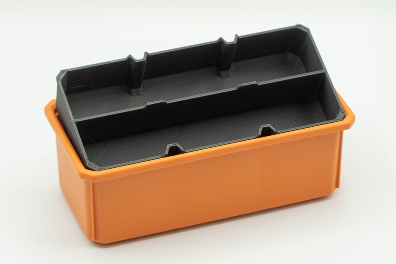 Puede incluir: Una caja de almacenamiento de pl&aacute;stico naranja con un inserto de pl&aacute;stico negro que tiene divisores. La caja est&aacute; vac&iacute;a.