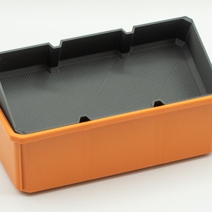 Puede incluir: Una caja de almacenamiento de pl&aacute;stico naranja con un inserto de pl&aacute;stico negro. El inserto tiene divisores para separar los art&iacute;culos.