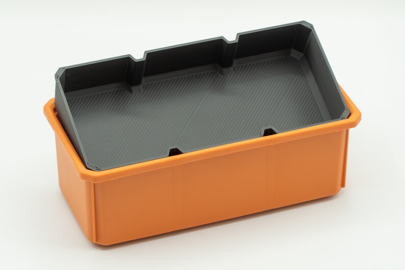 Puede incluir: Una caja de almacenamiento de pl&aacute;stico naranja con un inserto de pl&aacute;stico negro. El inserto tiene divisores para separar los art&iacute;culos.