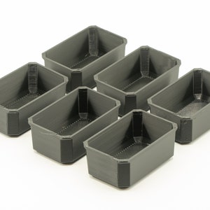 May include: Six small, rectangular, gray plastic containers. The containers are empty and have a textured surface.