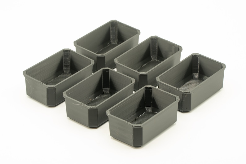 May include: Six small, rectangular, gray plastic containers. The containers are empty and have a textured surface.