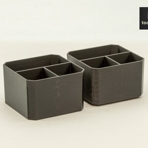 May include: Two grey plastic desk organisers with four compartments each. The organisers are made of a textured plastic and have a rectangular shape.
