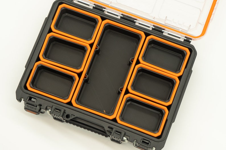 Puede incluir: Una caja de almacenamiento de pl&aacute;stico negro con un borde naranja y m&uacute;ltiples compartimentos. La caja est&aacute; abierta y los compartimentos est&aacute;n vac&iacute;os.