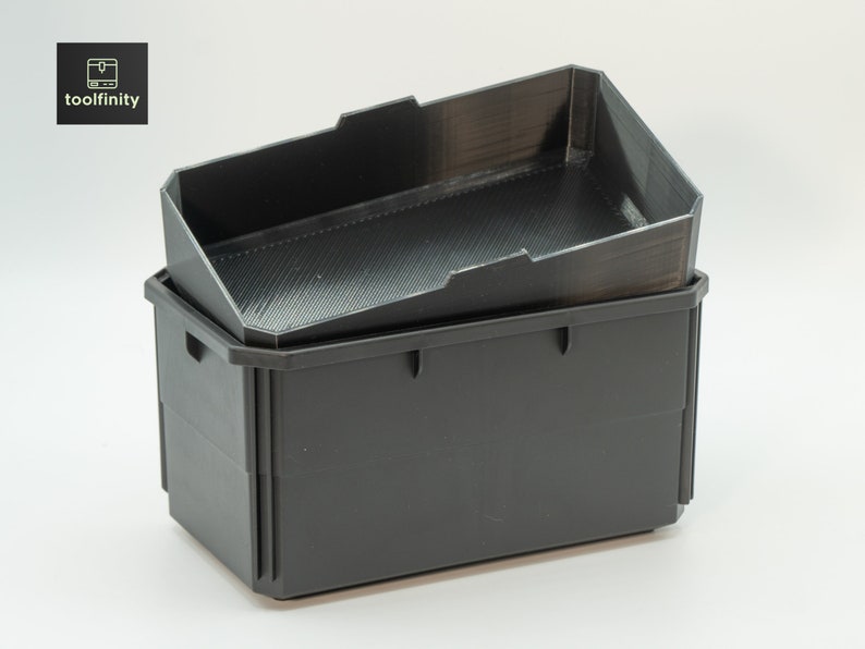 Op de afbeelding: Tweedelige zwarte opbergcontainers. De bovenste container is schuin met een gestructureerd interieur. De onderste container is rechthoekig met handgrepen. Het Toolfinity-logo staat in de linkerbovenhoek.