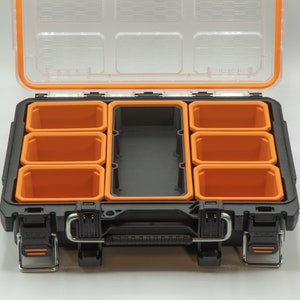 Puede incluir: Caja de herramientas de pl&aacute;stico negra y naranja con tapa transparente y varios compartimentos extra&iacute;bles. La caja de herramientas est&aacute; abierta y los compartimentos est&aacute;n vac&iacute;os.