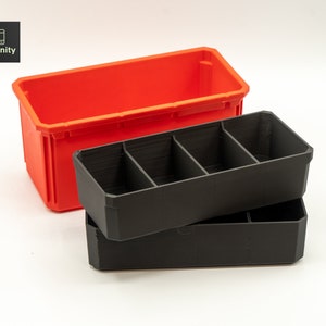 Puede incluir: Dos contenedores de almacenamiento de plástico, uno rojo y otro negro. El contenedor negro tiene cuatro compartimentos y está apilado encima del contenedor rojo.