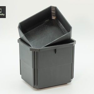 Puede incluir: Juego de dos contenedores de almacenamiento de color gris oscuro. El contenedor inferior es una caja rectangular con una superficie ligeramente texturizada. El contenedor superior es una bandeja con un patrón diagonal texturizado. El logotipo "toolfinity" está en la esquina superior izquierda.