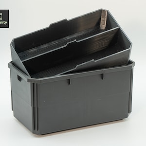 Puede incluir: Una caja de almacenamiento de plástico negro con un inserto de plástico negro que tiene dos compartimentos. El inserto está sentado dentro de la caja.