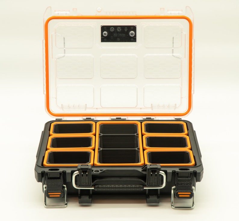 Puede incluir: Una caja de almacenamiento de pl&aacute;stico negro con un borde naranja y una tapa transparente. La caja tiene nueve compartimentos para organizar art&iacute;culos peque&ntilde;os.