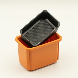 May include: A black plastic storage bin with a smaller black plastic bin inside. The larger bin is orange.