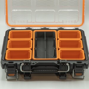 Puede incluir: Una caja de herramientas de pl&aacute;stico negra con varios compartimentos naranjas. La caja de herramientas tiene una tapa transparente y una manija de transporte.