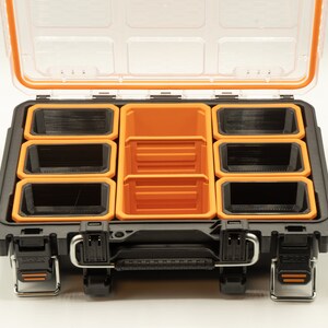 May include: A black plastic storage box with an orange lid and multiple removable orange and black compartments. The box is open and the compartments are visible.