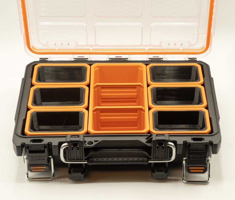 May include: A black plastic storage box with an orange lid and multiple removable orange and black compartments. The box is open and the compartments are visible.