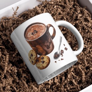 May include: White ceramic mug with a brown and white illustration of a mug of hot chocolate, a spoon, and chocolate chip cookies.