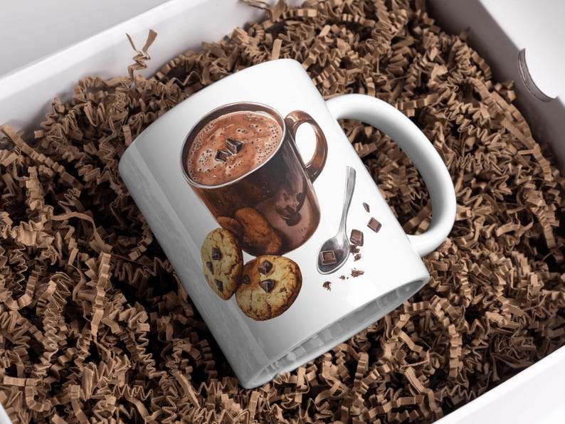 May include: White ceramic mug with a brown and white illustration of a mug of hot chocolate, a spoon, and chocolate chip cookies.