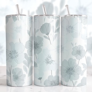 Könnte beinhalten: Drei isolierte Edelstahlbecher mit floralen Mustern. Die Becher haben einen weißen Hintergrund mit einem sich wiederholenden Muster aus hellblauen Blumen und Blättern. Jeder Becher hat einen durchsichtigen Kunststoffstrohhalm und einen silbernen Deckel.