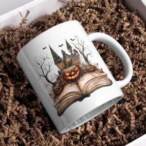 May include: White ceramic mug featuring a Halloween-themed design. The illustration depicts a spooky castle, jack-o'-lanterns, and bats, set against a backdrop of bare trees and an open book. The mug is presented in a white box with brown paper filler.