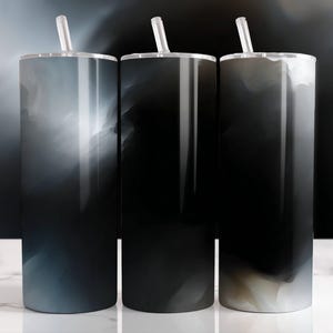 Puede incluir: Tres vasos altos y cilíndricos con tapas y pajitas. Cada vaso presenta un diseño abstracto oscuro con tonos de negro, gris y blanco, que se asemeja a un cielo nublado. Los vasos se exhiben sobre una superficie blanca.