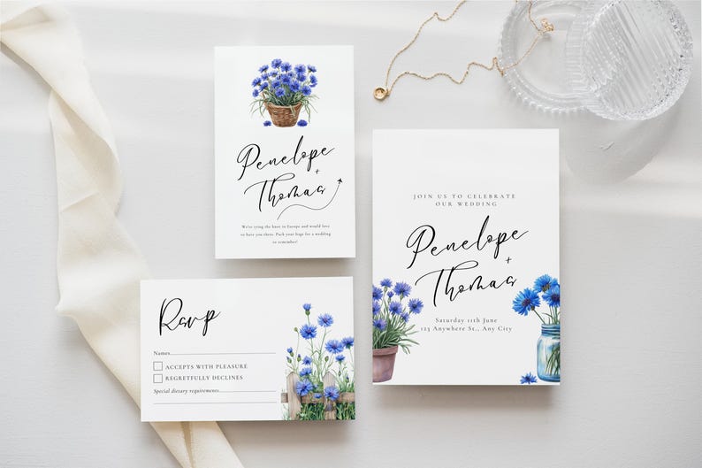 May include: A set of wedding stationery with a floral design. The invitation, RSVP card, and details card feature blue watercolour flowers and the names "Penelope + Thomas". The suite has a rustic, floral theme.