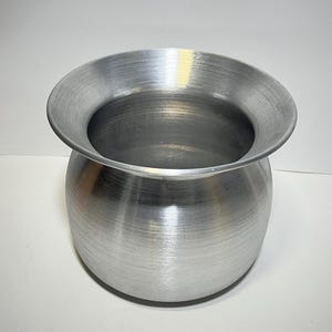 Peut inclure: Une casserole en aluminium argentée avec un bord large et plat et un corps arrondi. La casserole a une finition brossée.