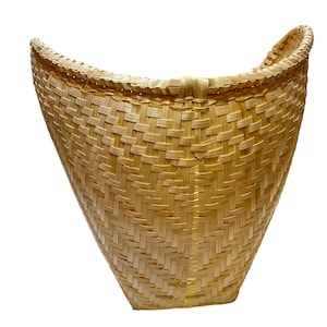 May include: A woven, light brown, basket with a rounded, open top and a handle on each side. The basket is made of natural materials and has a traditional design.