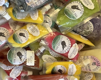 May include: A collection of WV Candle Co. squeezy wax pouches in various colors and scents. Each clear plastic pouch features a white label with the brand logo, a map of West Virginia, and specific scent names like Witches Brew, Sunshine & Silk, and Juicy Watermelon.