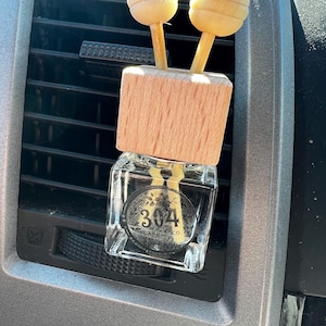 May include: A clear glass bottle with a wooden lid and two wooden sticks with round wooden balls on the ends. The bottle has a black label with the text "304 CANDLE CO."