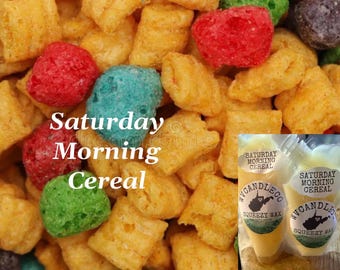 Könnte beinhalten: Eine Ansammlung bunter, knuspriger Getreidestücke in Gelb-, Rot-, Grün- und Blautönen, überlagert mit dem Text "Saturday Morning Cereal". Zwei durchsichtige Beutel mit "Saturday Morning Cereal" Squeezy-Wachs sind unten rechts zu sehen.