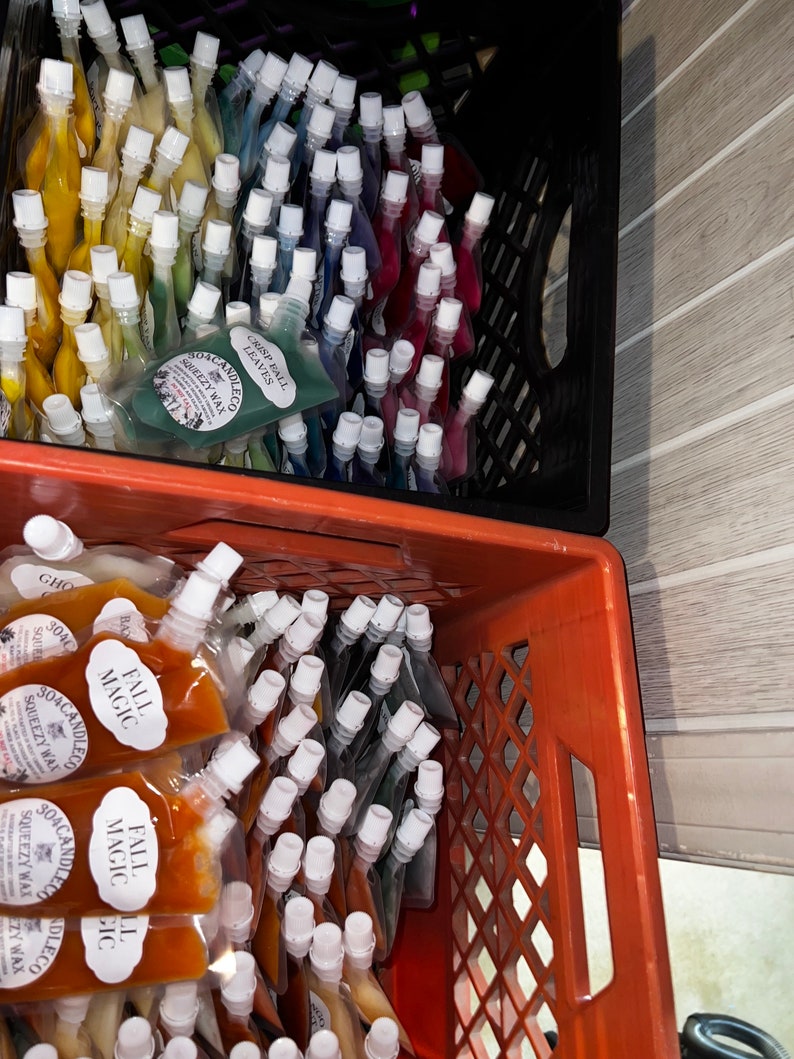 May include: Two crates filled with small, clear plastic pouches containing colorful wax melts. The pouches are labeled "Soacandle.co" and "Squeezy Wax". The top crate has pouches labeled "Crisp Ball Leaves" and the bottom crate has pouches labeled "Fall Magic".