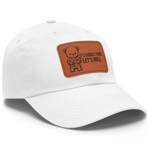 May include: White baseball cap with a brown leather patch. The patch features a cartoon bear in a karate uniform and the text "IT'S CUDDLE TIME LET'S ROLL". The cap has a curved brim and a button on top.