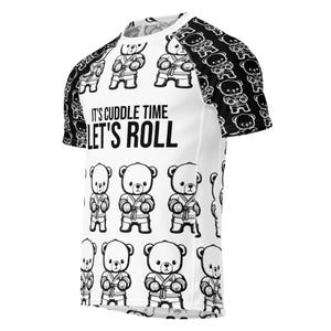 May include: White t-shirt with black and white bear illustrations in karate uniforms. The shirt features the text "IT'S CUDDLE TIME LET'S ROLL" in black. The sleeves have a repeating pattern of black and white bear illustrations.