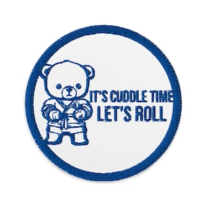 May include: Embroidered patch with a blue outline and a white center. The patch features a blue cartoon bear in a karate uniform and the text "IT'S CUDDLE TIME LET'S ROLL".