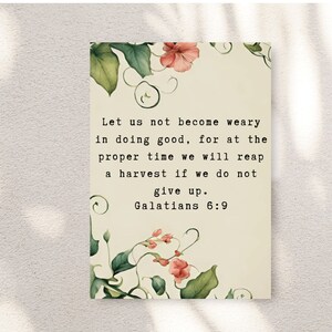 May include: A rectangular print with a cream background, featuring the text "Let us not become weary in doing good... Galatians 6:9." Floral watercolor illustrations in pink and green adorn the edges, creating a decorative border.